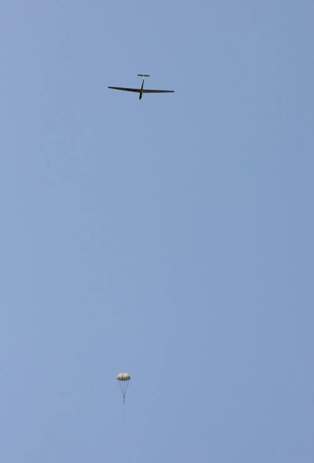 A glider high overhead in a pale blue sky, climbing away on a winch launch