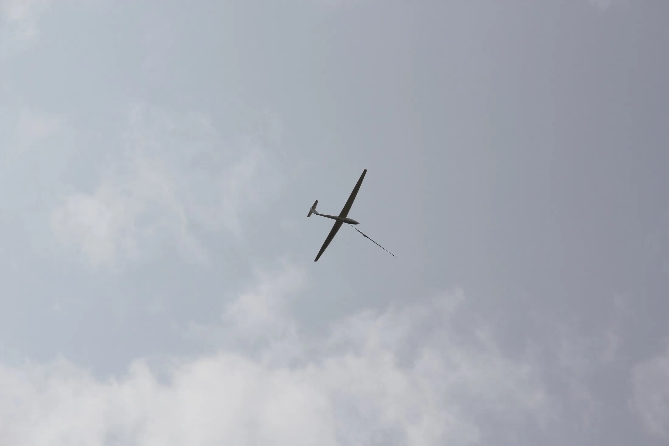 The silhouette of a two-seat glider on a winch cable, banked against towering clouds