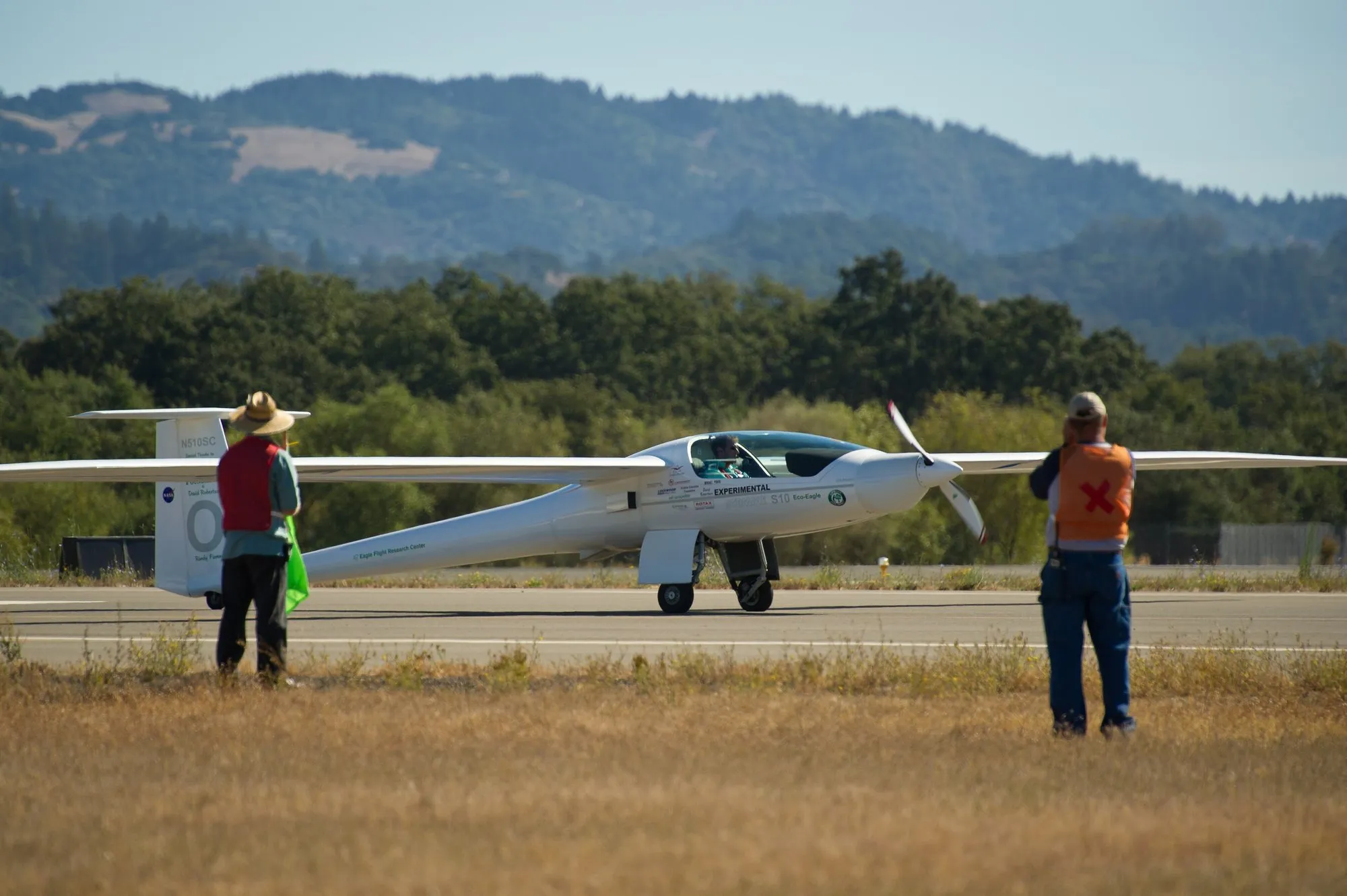 A Stemme S10 motor glider on the runway, marshals in high-vis watching it prepare to take off
